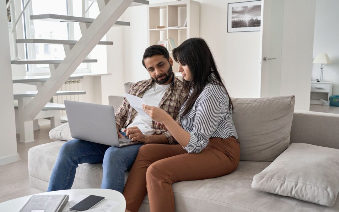 a couple looks at their financial statements and their laptop while sitting on a couch